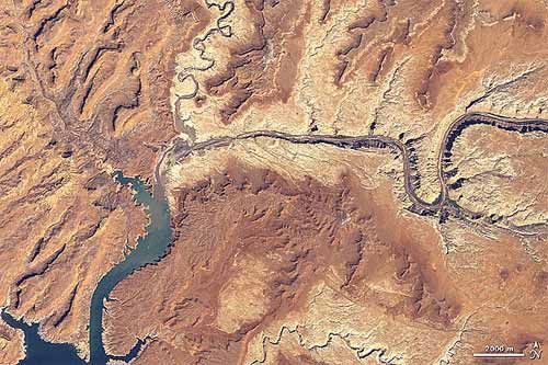 An aerial view showcases the Colorado River winding through a desert landscape, featuring rocky terrain and sparse vegetation.