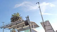 Outdoor stage with scaffolding, speakers, and a light pole under a clear blue sky with a palm tree in the background—like the vibrant setup at Treasure Island Music Festival, where the focus is all about going green.